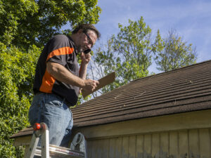 Contractor on ladder with cell phone figuring out hail damage repair costs for customer.