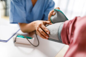 A close up photograph of an unrecognizable female nurse measuring blood pressure of a woman.