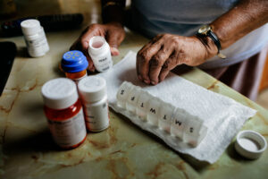 A photo of an older man sorting medicine into a weekly pill organizer.