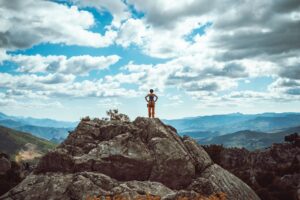 Female leader mountain climber is celebrating her success and watching the beautiful scenery of forest and mountain range