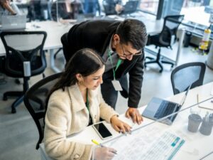 Businessman leader helping young woman at a desk in the office