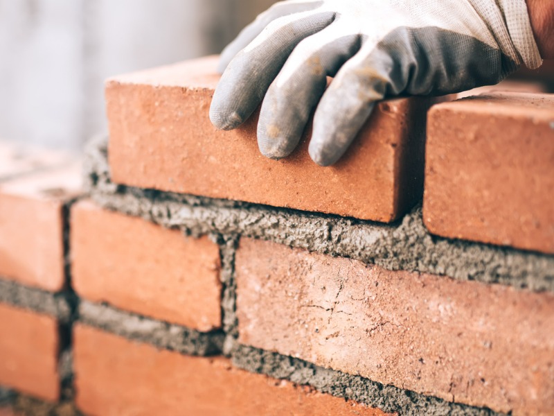 Close up of an industrial bricklayer installing bricks to build back on a construction site
