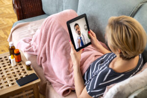 Mature woman using digital tablet for conversation with her doctor. She is lying on the couch in the living room and has video call and consultation with her doctor.