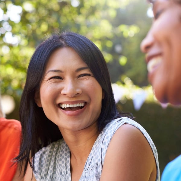 A close-up image of a mature woman laughing and enjoying a meal outdoors.