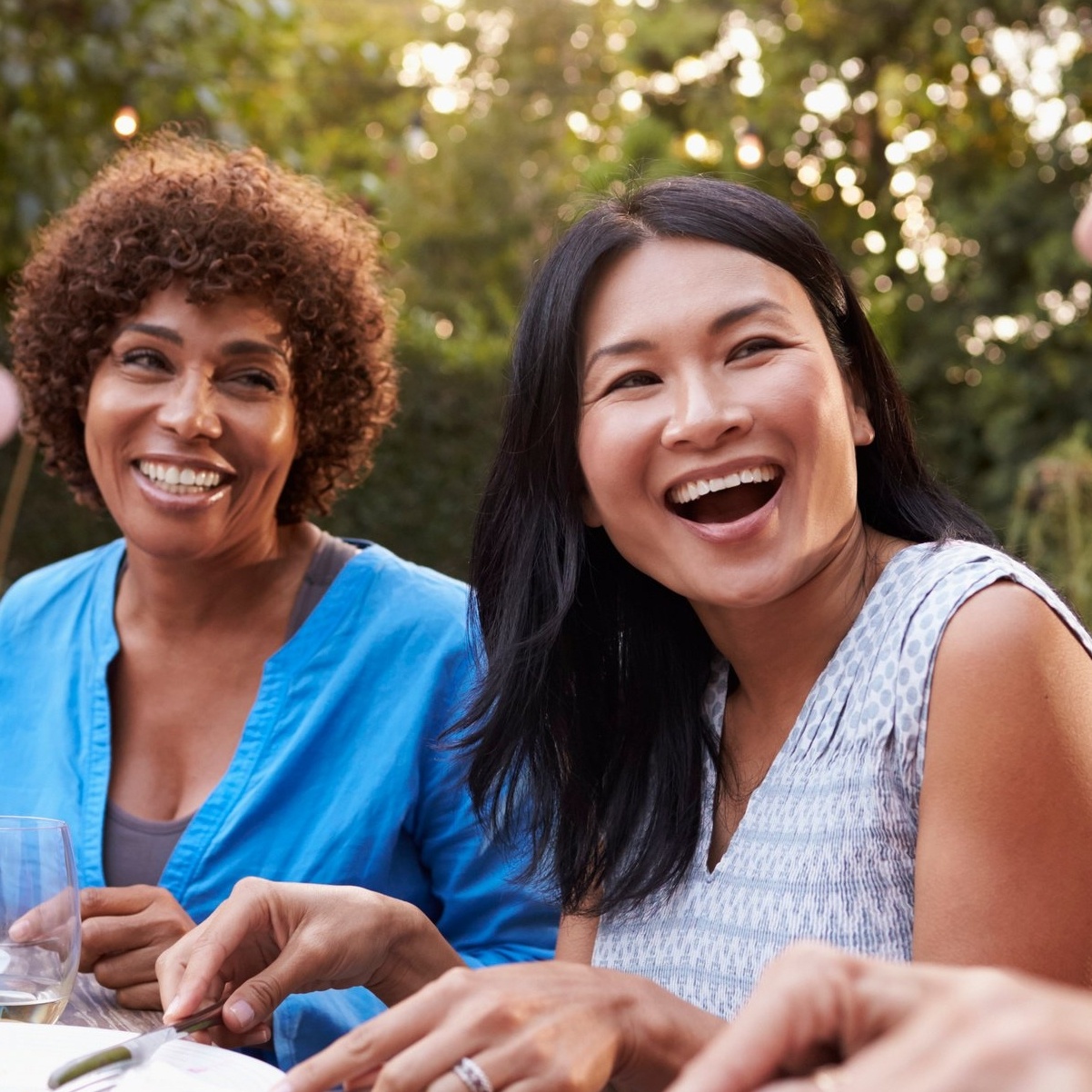 Two mature women laughing and enjoying a meal outdoors.