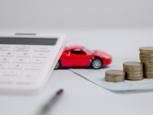 Red toy car between a stack of coins and a calculator