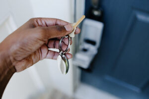 The photo shows a person holding house keys in their left hand. They prepare to unlock the door in front of them.