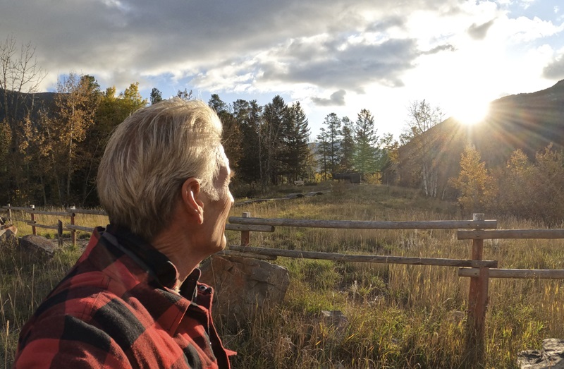 Mature man relaxes fence in meadow at sunrise