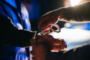 Policeman putting handcuffs on young criminal's hands at night.