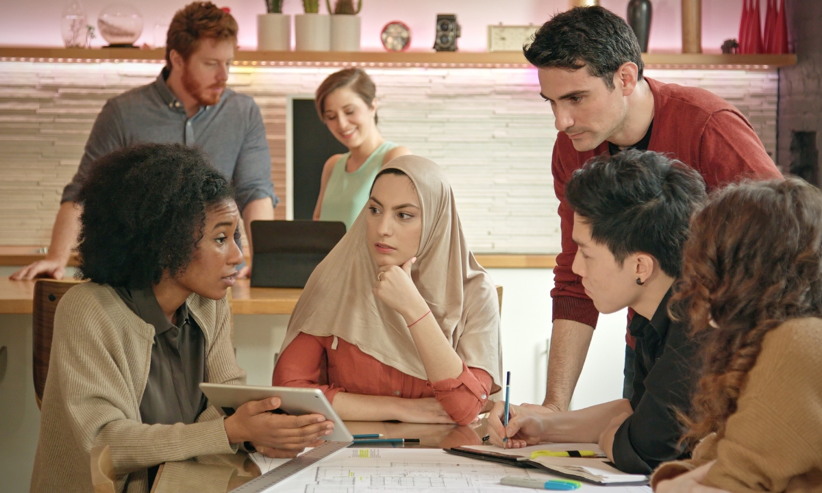 small business employees gathered around a table speaking with a woman with a tablet