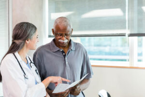 The senior adult man looks at the brochure in his hands as the mid adult female doctor explains the options detailed there.