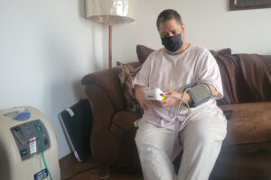 A man seated on his coach at home measures his blood pressure.