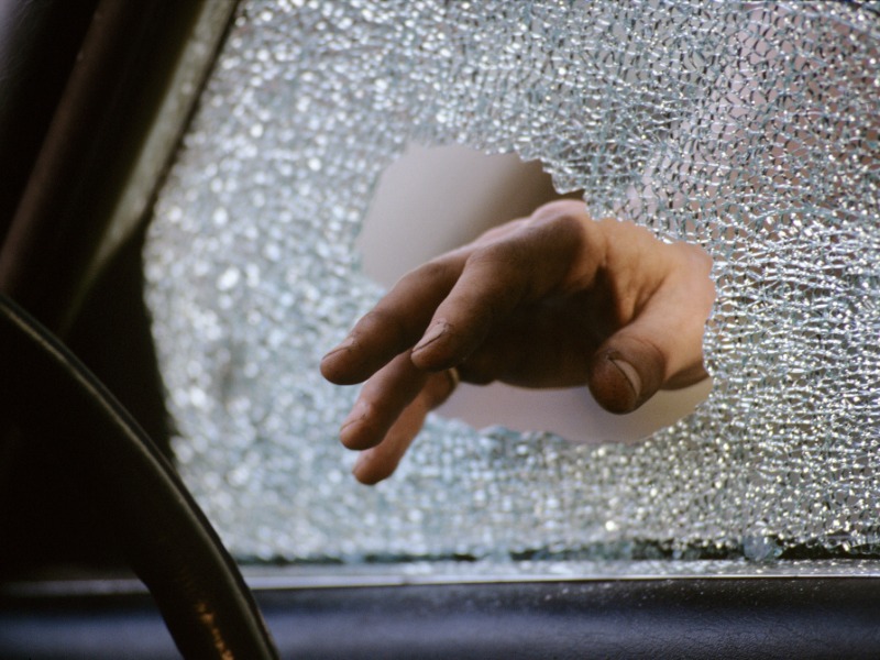 A person's hand breaking the window of a vehicle for the purpose of auto theft