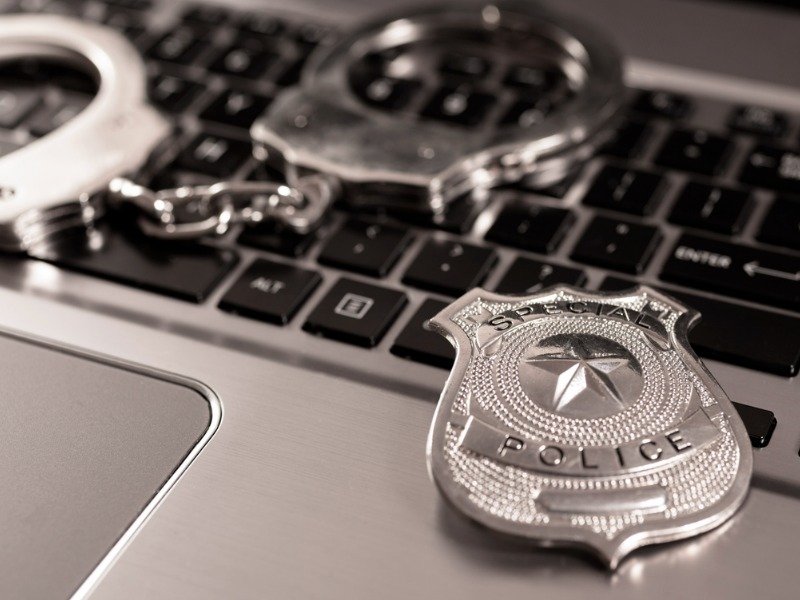 Police badge and handcuffs on a computer to represent regulators cracking down on computer crime