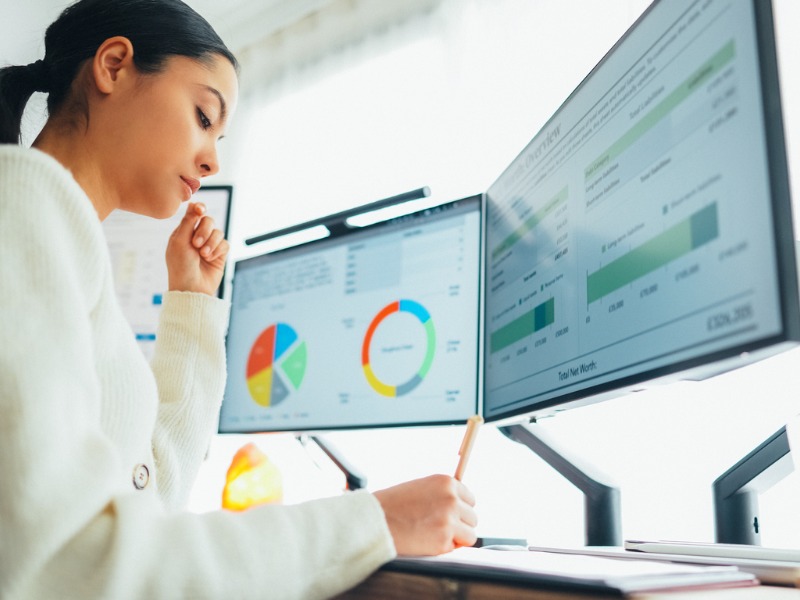 Woman working with two desktop screens that are displaying circle and bar graph data