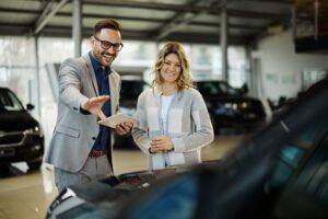 Happy salesman selling the car to his female customer in a showroom.