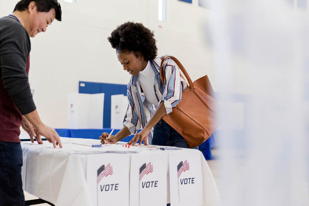 A young woman is helped to sign in by a volunteer at a polling place