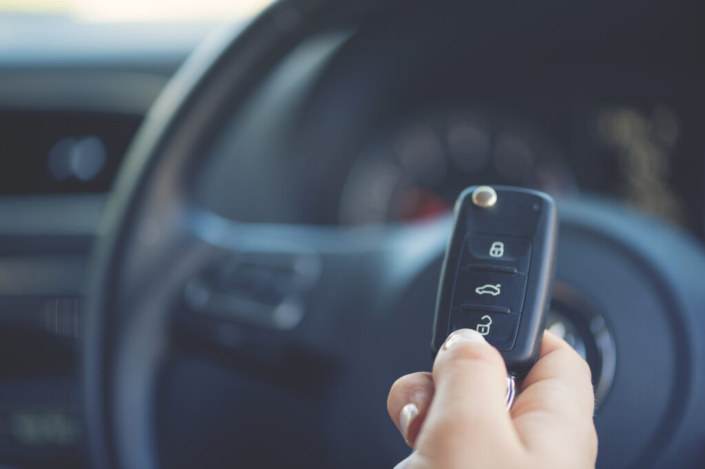 Woman holding an auto key. The steering wheel and dashboard are in the background.