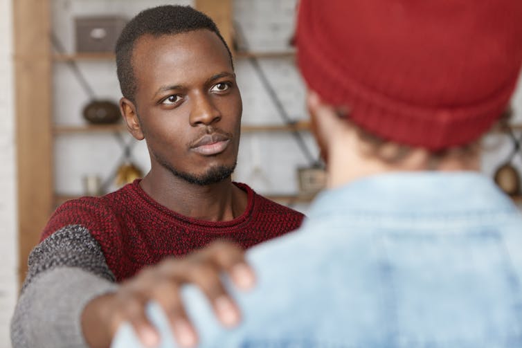 A young man reaching out with his hand on the shoulder of another young man with his back to the camera