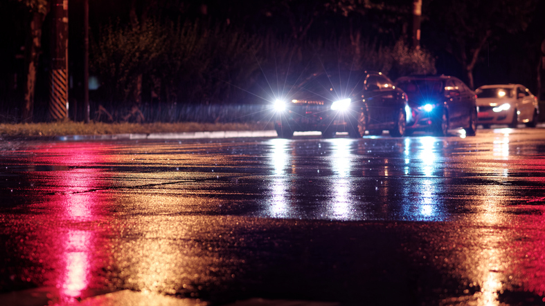 Rainy night in city, cars waiting on wet road because of red traffic light, rain was illuminated by the headlights of cars, focused on the asphalt road.