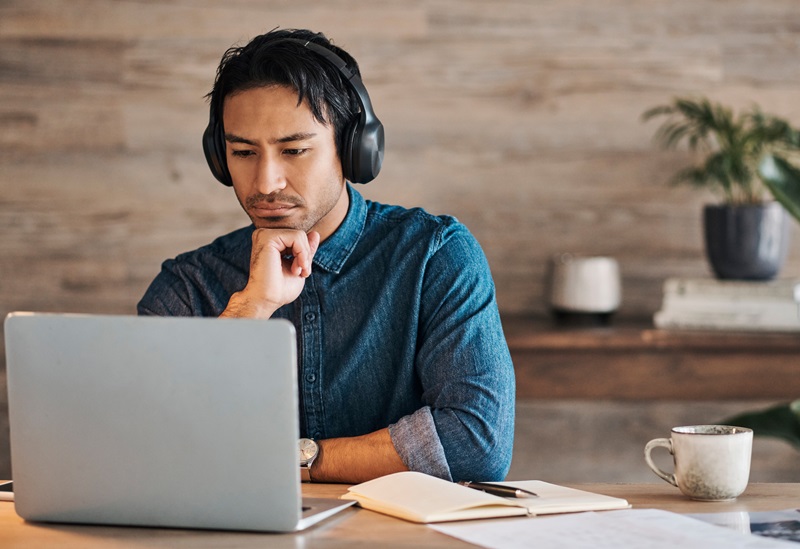 Businessman at a desk working on project with headphones and laptop and coffee on table