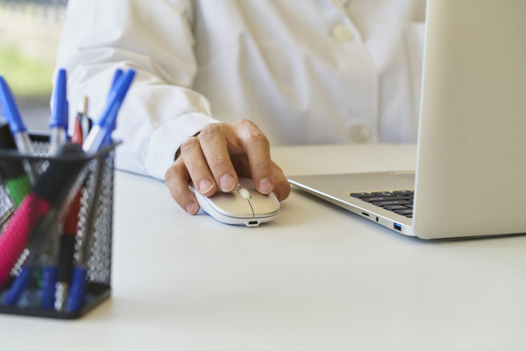 A close up photo of a person's hand on computer mouse while they use a laptop on a desk.