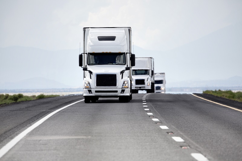 Three white trucks in a convoy on an interstate highway