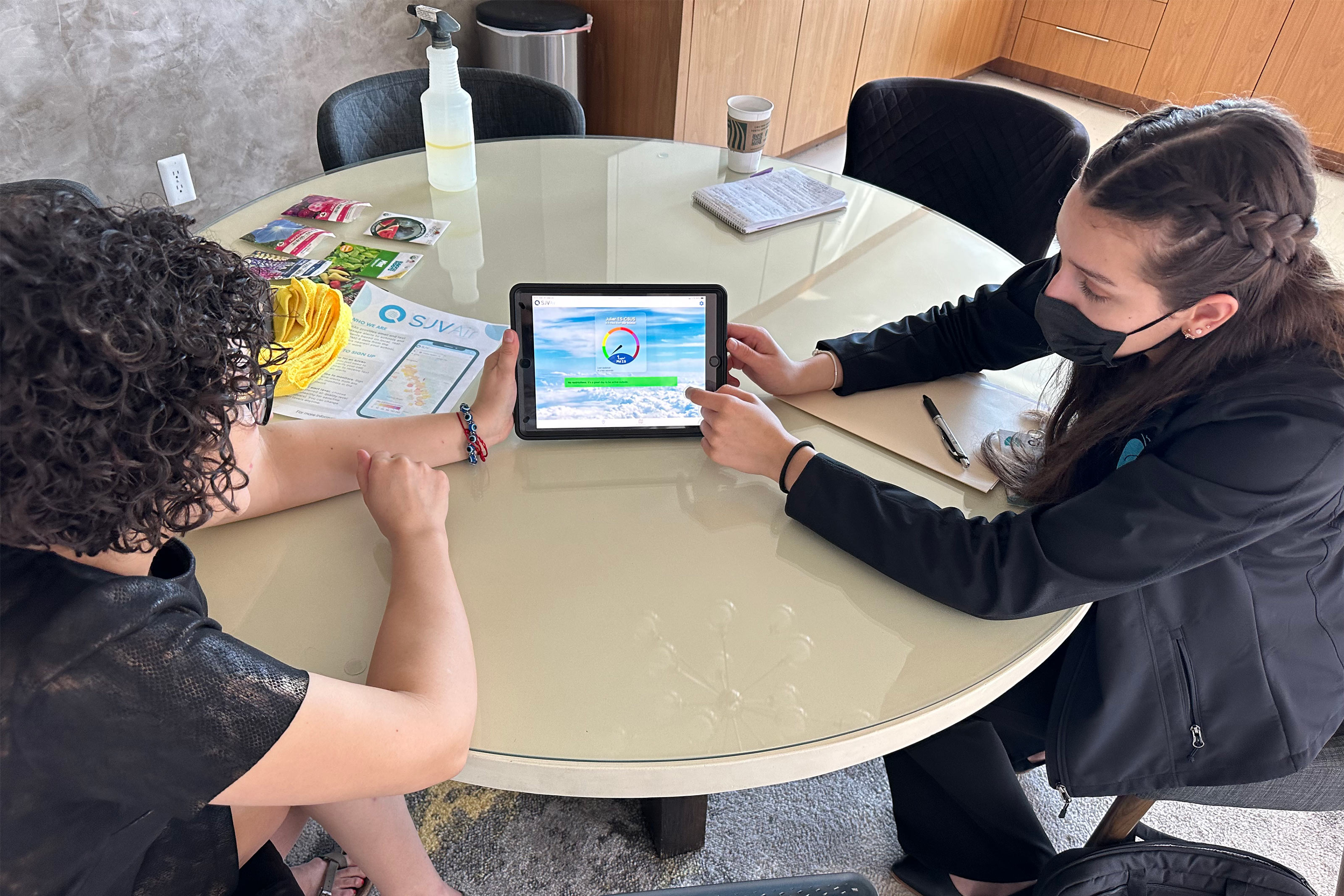 A photo of a mother and a community health worker sitting at a table and looking at a tablet.