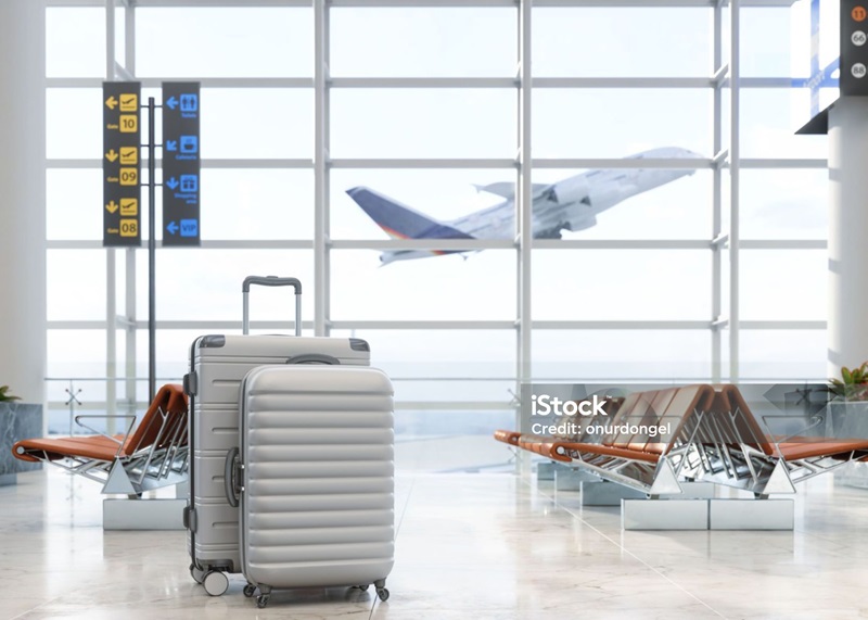 Travel bags in waiting area of airport in the foreground. Plane taking off through the window