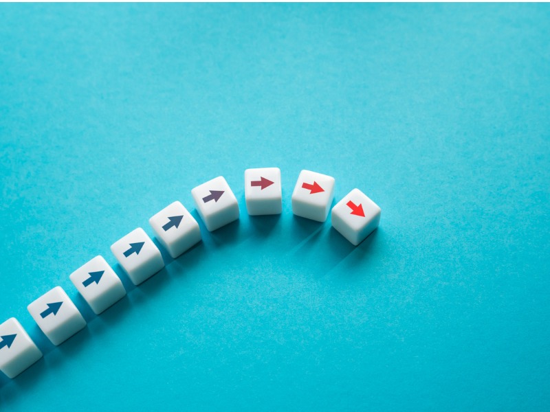 white dice with directional arrows on a bright turquoise background. Most arrows point right and ascend in height, while the last two maintain the same level.