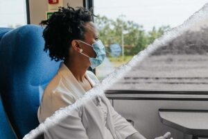 A woman wearing a mask looks out the window of a train on her commute.