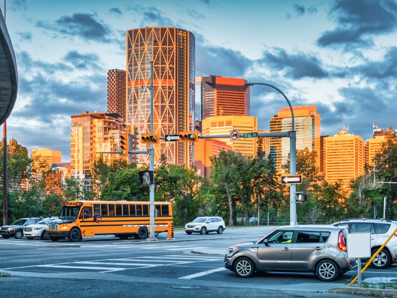 "Sunset over downtown Calgary, Alberta, with cars and a school bus at an intersection. Image of Alberta auto traffic in urban setting.