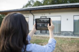 Home insurance inspector looking at a house and using a tablet.