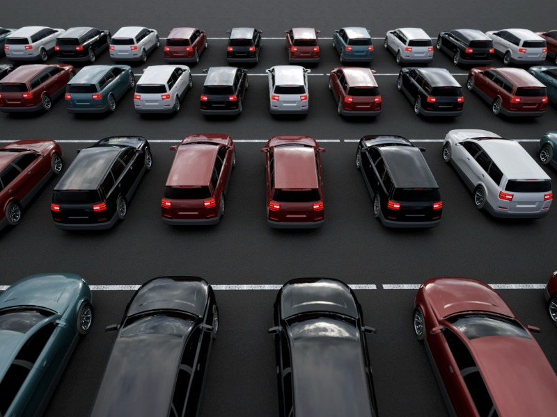 Aerial shot of four rows of cars of various colours lined up in darkly lit parking lot