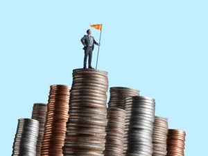 A man stands up tall while holding a flag on top of a large stack of coins in front of a blue background