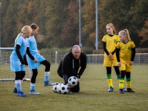 Father coaching soccer to his daughter's team at a football game on a sunny autumn day