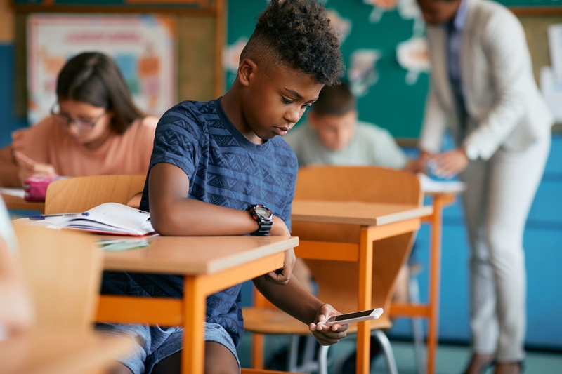 Black elementary student typing text message while secretly using cell phone during a class at school.