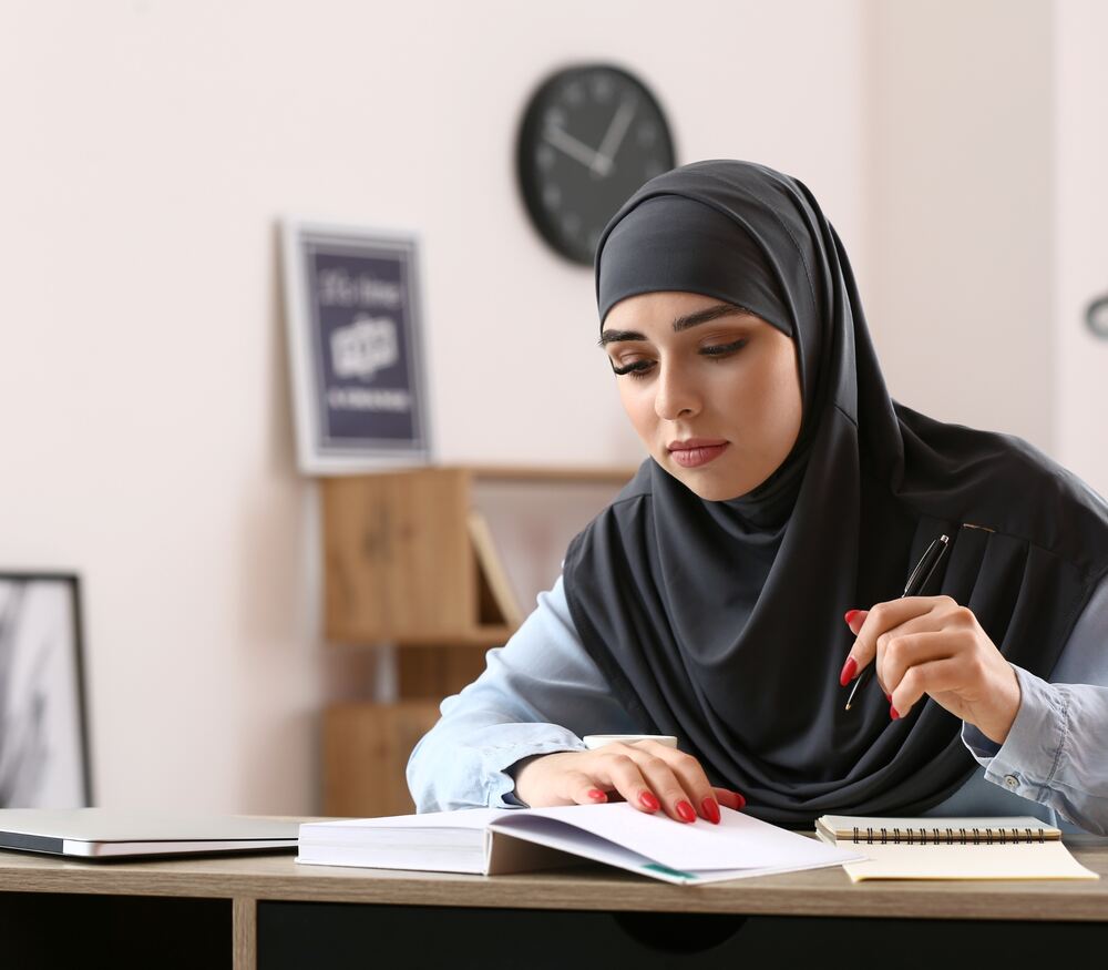 Woman wearing hijab writing on book