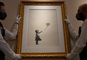 Art handlers display an artwork by Banksy called 'Girl with Balloon-Colour AP (Gold)' at Christie's auction rooms in London, Friday, Sept. 17, 2021. The artwork estimated at 800,000-1,200,000 UK Pounds (1,200,000-1,700,000 US Dollars) will be up for auction in the Christie's Sept. online only sales. (AP Photo/Kirsty Wigglesworth)