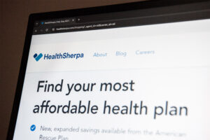 A photo of a computer screen with HealthSherpa's website open. The screen shows the company logo and text that reads, "Find your most affordable health plan."