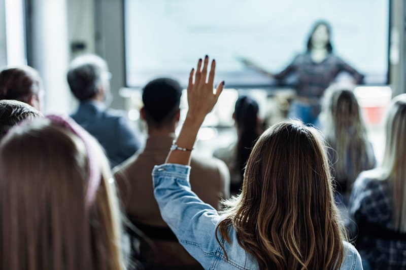 Back view of creative woman asking a question on education event in the office.