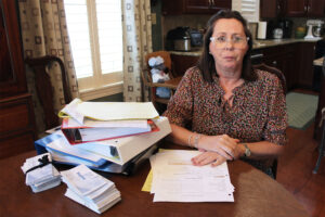 A photo of a woman sitting at a table with a pile of medical records and billing documents.