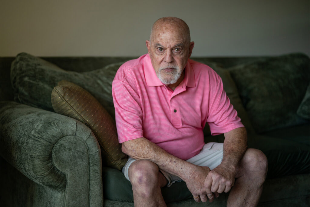 A photo of a man seated on his couch, looking at the camera.