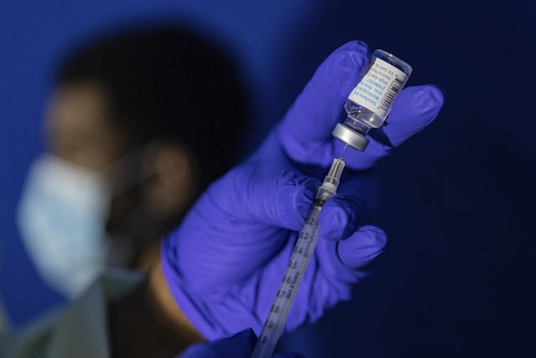 Health worker wearing blue gloves drawing up mpox vaccine into syringe