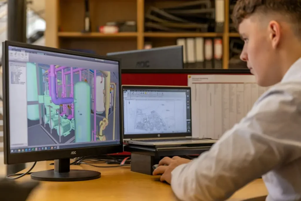 Person sitting at a desk looking at a computer screen showing a pipe network