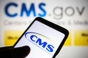 A photo of a phone with the CMS logo visible on its screen and in the background behind it.