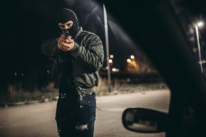 Masked thief is holding car owner at a gunpoint