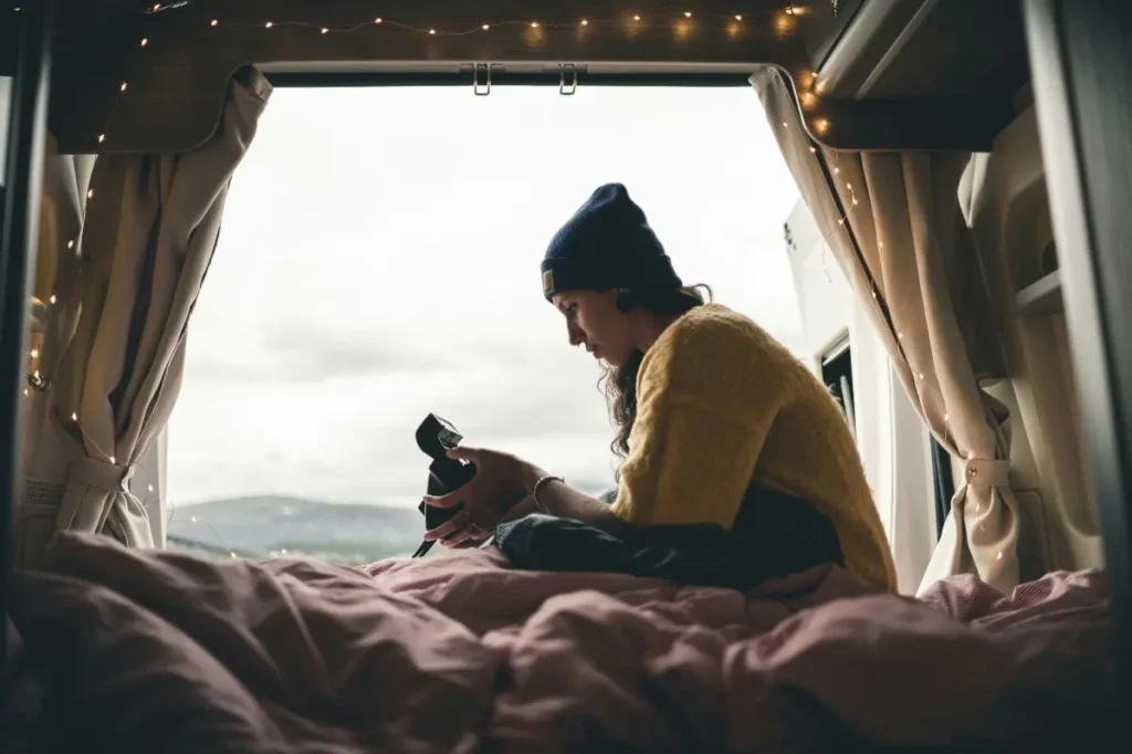 Woman sitting on her campervan bed with fairy lights looking at her camera