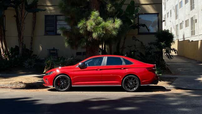 A side view of the kings red Jetta GLI parked on a street in front of a pine tree