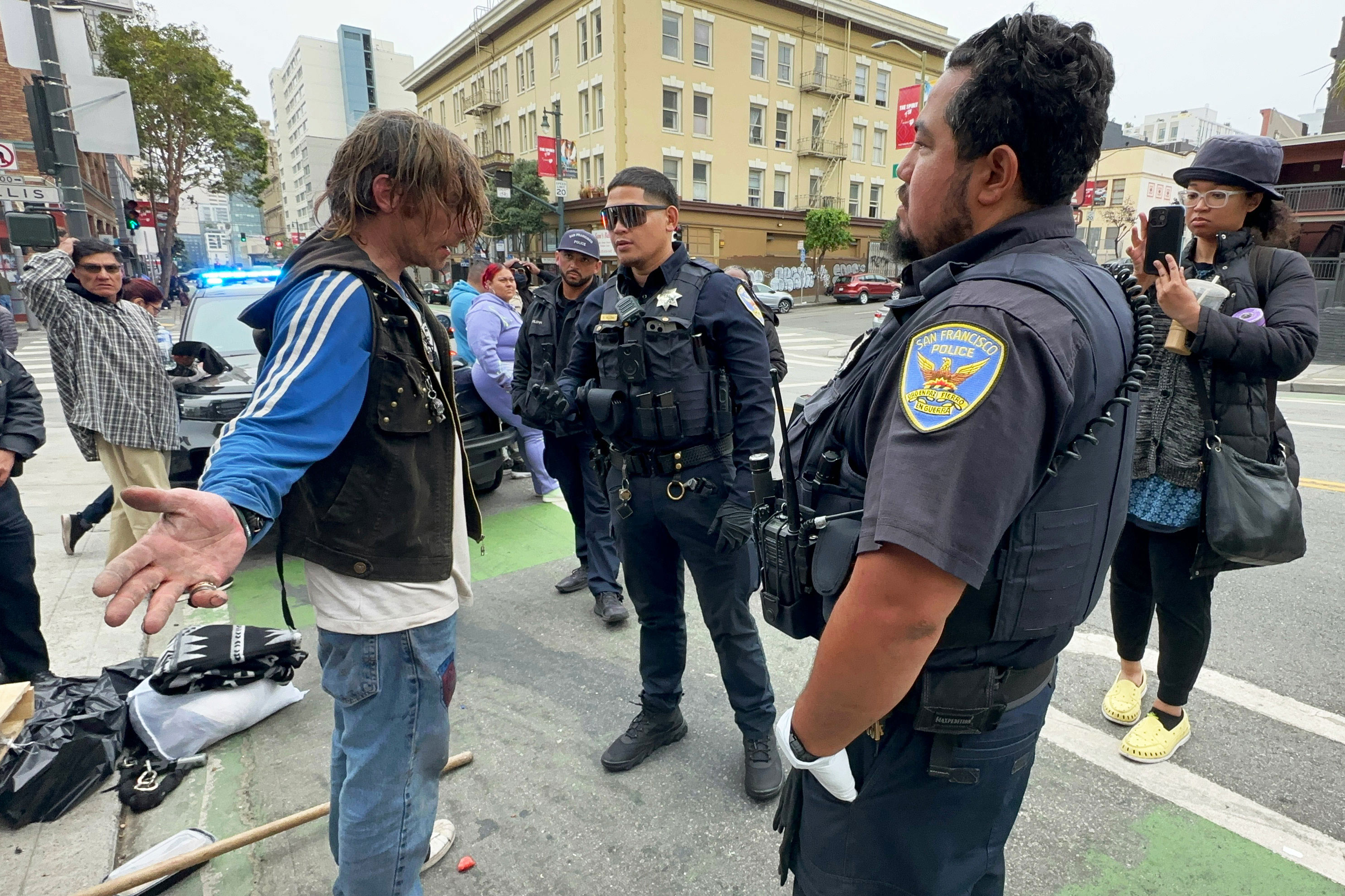 A photo of Andrew Douglass with his arms fanned out, speaking to police officers.